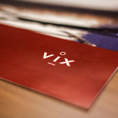 Bildet viser et nærbilde av VIX' logo, hvit på mørkerød bakgrunn, plassert på en trykksak.